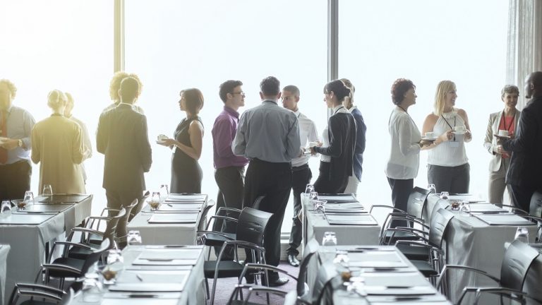 Group of people standing by windows of conference room, socializing during coffee break